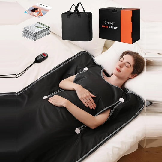 Portable infrared sauna blanket in black shown on a bed with wired controller, carrying bag, manuals, and EHINI product box